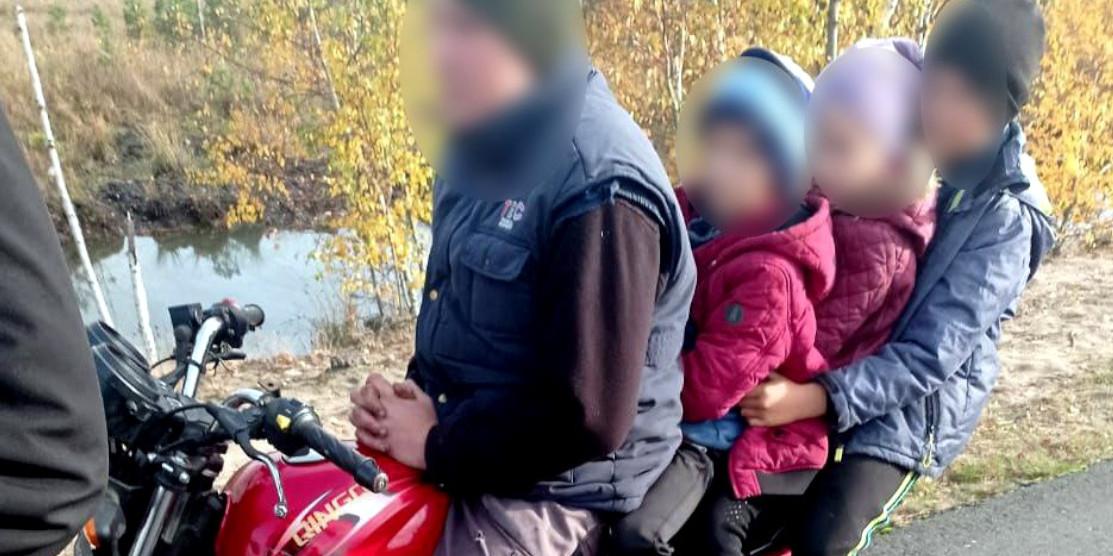 Батько перевозить на мотоциклі трьох малолітніх дітей.