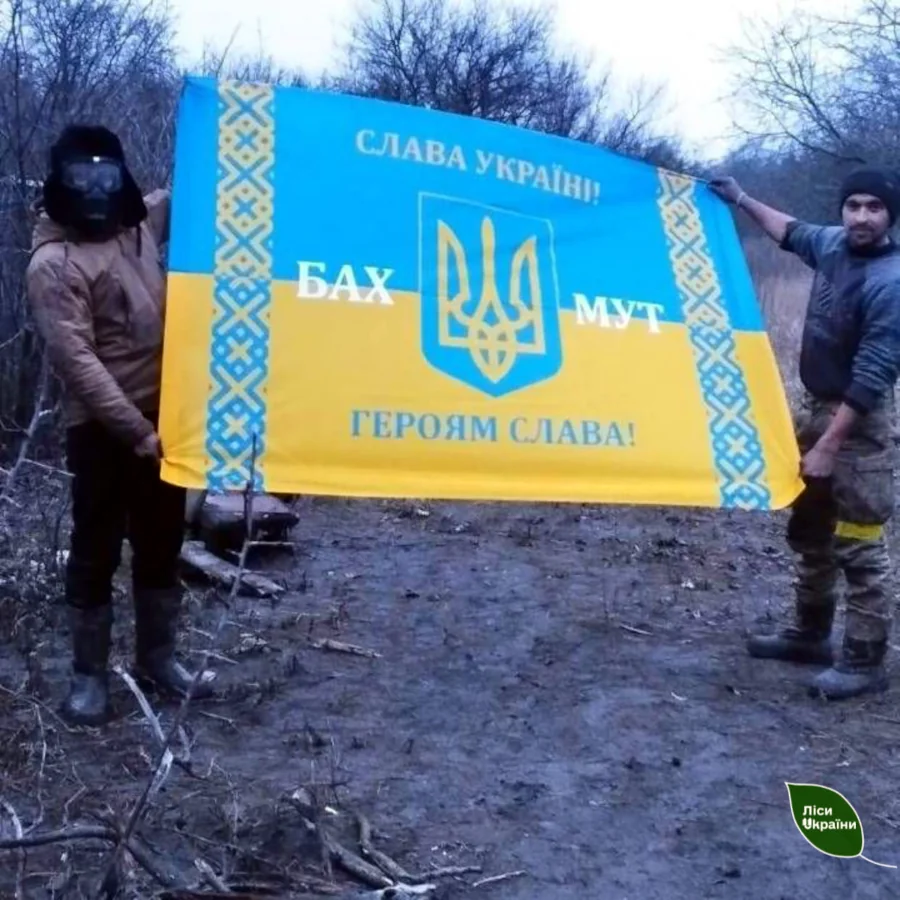 Два воїни тримають прапор України десь під Бахмутом.
