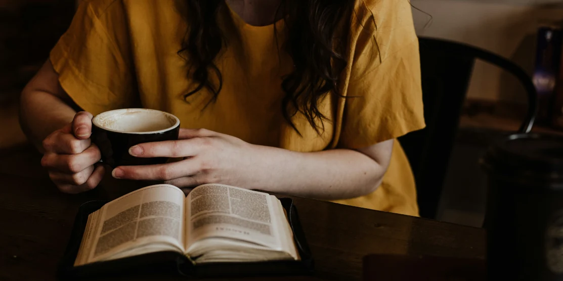 Дівчина читає книжку і п'є каву.