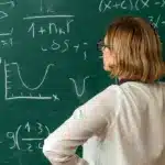 Вчителька стоїть перед шкільною дошкою й дивиться на діаграми.