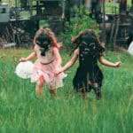 Дівчата біжать з повітряними кульками зеленим полем у протигазах.