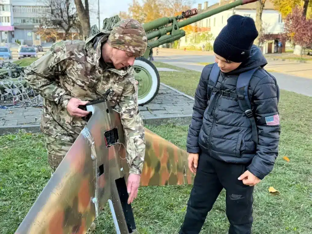 Михайло Снітчук показує уламки збитого російського безпілотника відвідувачу музею.