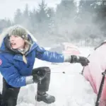 Жінка у зимовій куртці Canada Goose встановлює намет у суворих зимових умовах