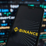Смартфон із логотипом криптовалютної біржі Binance на екрані на тлі цифрових даних та графіків.