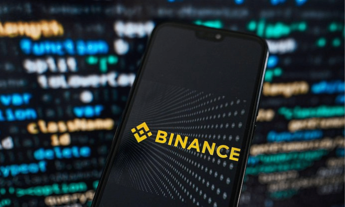 Смартфон із логотипом криптовалютної біржі Binance на екрані на тлі цифрових даних та графіків.