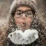 Дівчина дує на сніг у долонях.