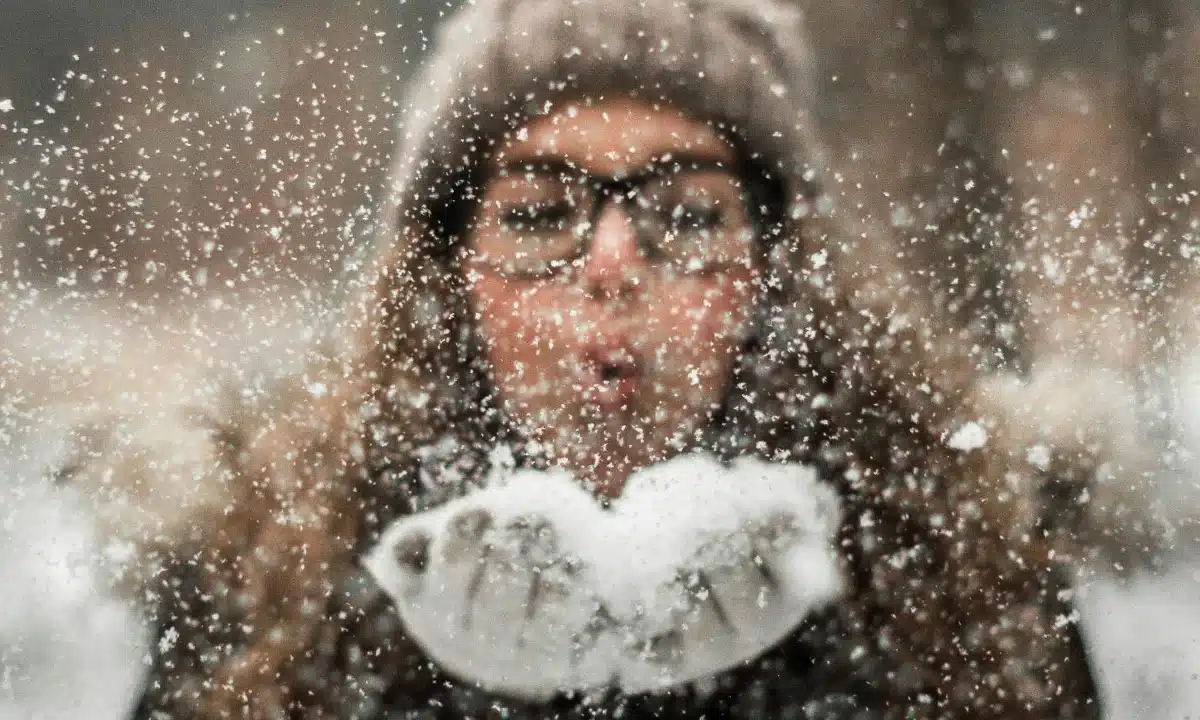 Дівчина дує на сніг у долонях.