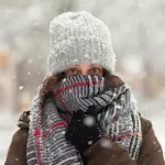 Дівчина закутана у шалик на засніженій вулиці.