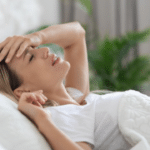 Жінка лежить у ліжку з рукою на чолі, відчуває головний біль або нездужання вдома.