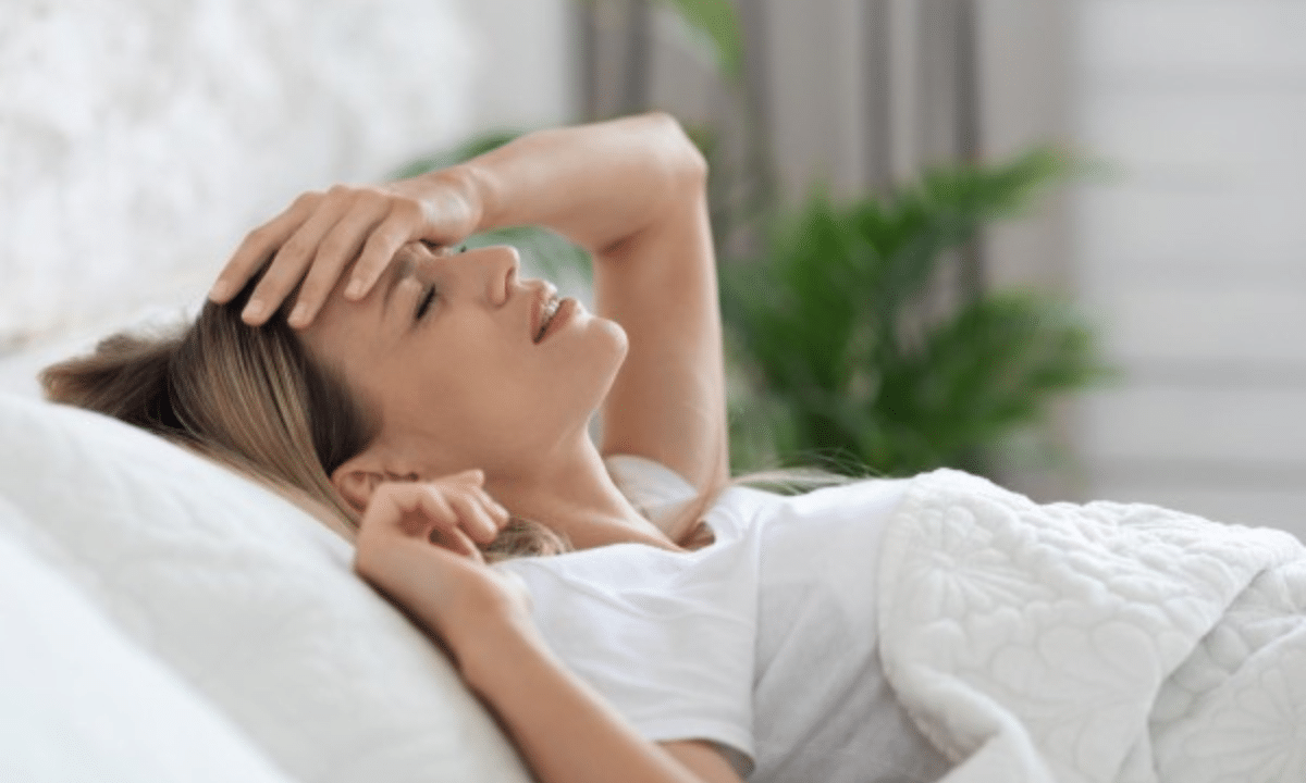 Жінка лежить у ліжку з рукою на чолі, відчуває головний біль або нездужання вдома.