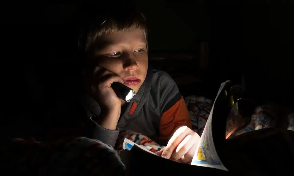 Графіки відключень електроенергії на Рівненщині у четвер, 11 грудня Хлопчик читає книжку з ліхтариком.