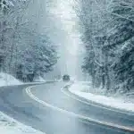 Авто їде мокрою дорогою через засніжений ліс.