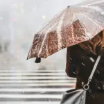 Жінка стоїть на вулиці з парасолькою і падає сніг.
