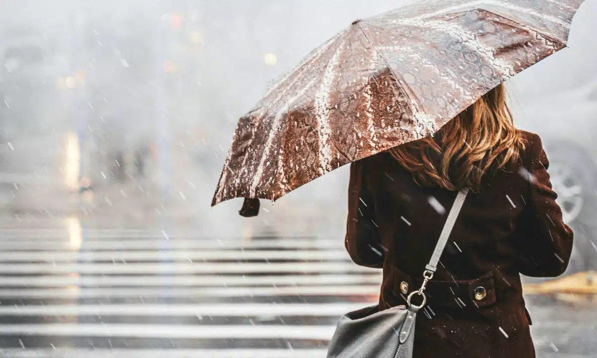 Жінка стоїть на вулиці з парасолькою і падає сніг.