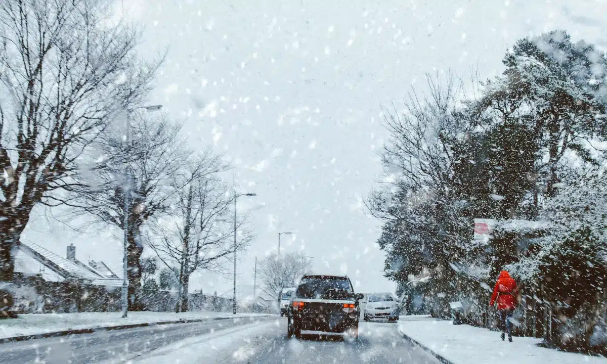 Авто минає перехожу в червоній куртці по засніженій дорозі.