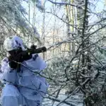 Боєць ССО в камуфляжі позує з гвинтівкою у лісі.