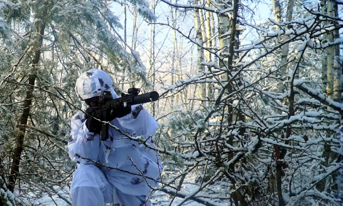 Боєць ССО в камуфляжі позує з гвинтівкою у лісі.