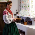 Дівчинка в українському традиційному вбранні стоїть біля печі.