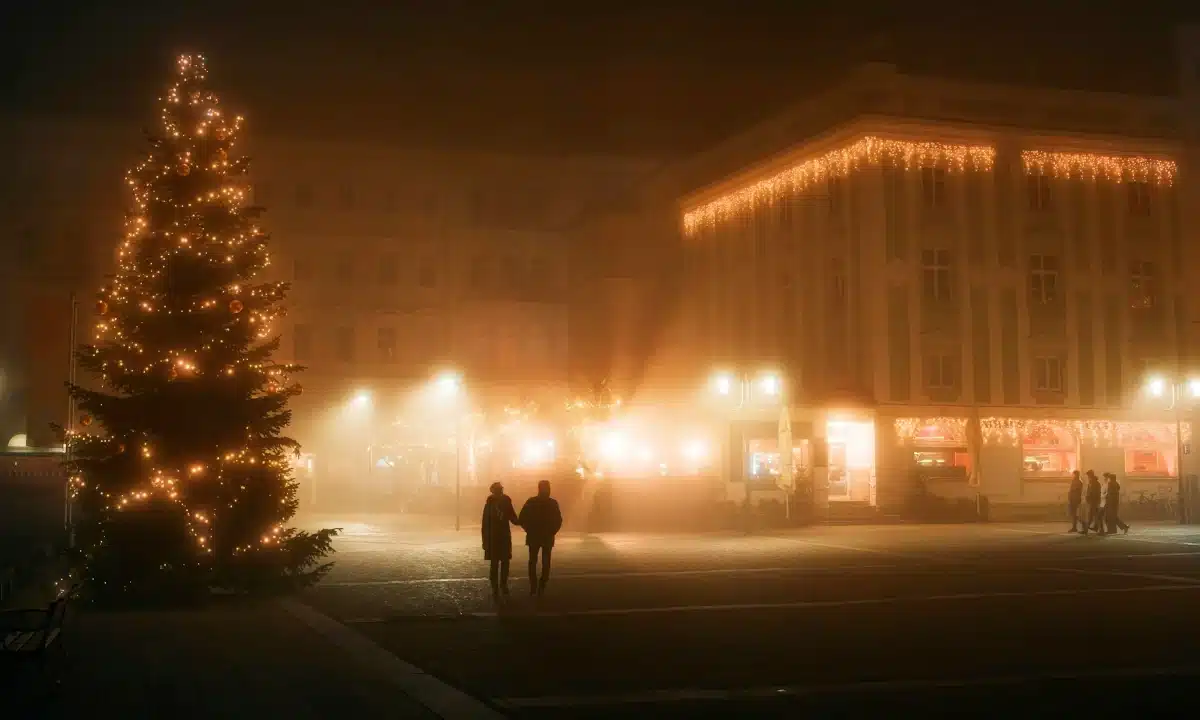 Новорічна ялинка на нічній туманній площі, сяють святкові вогні й ходять люди.