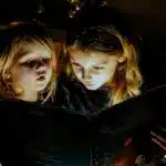 Дівчата читають книжку з ліхтариком.