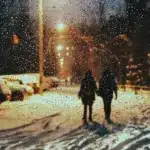 Двоє людей ідуть по снігу, падає дощ.