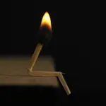 Сірник, зламаний у формі чоловіка, запалений на столі.