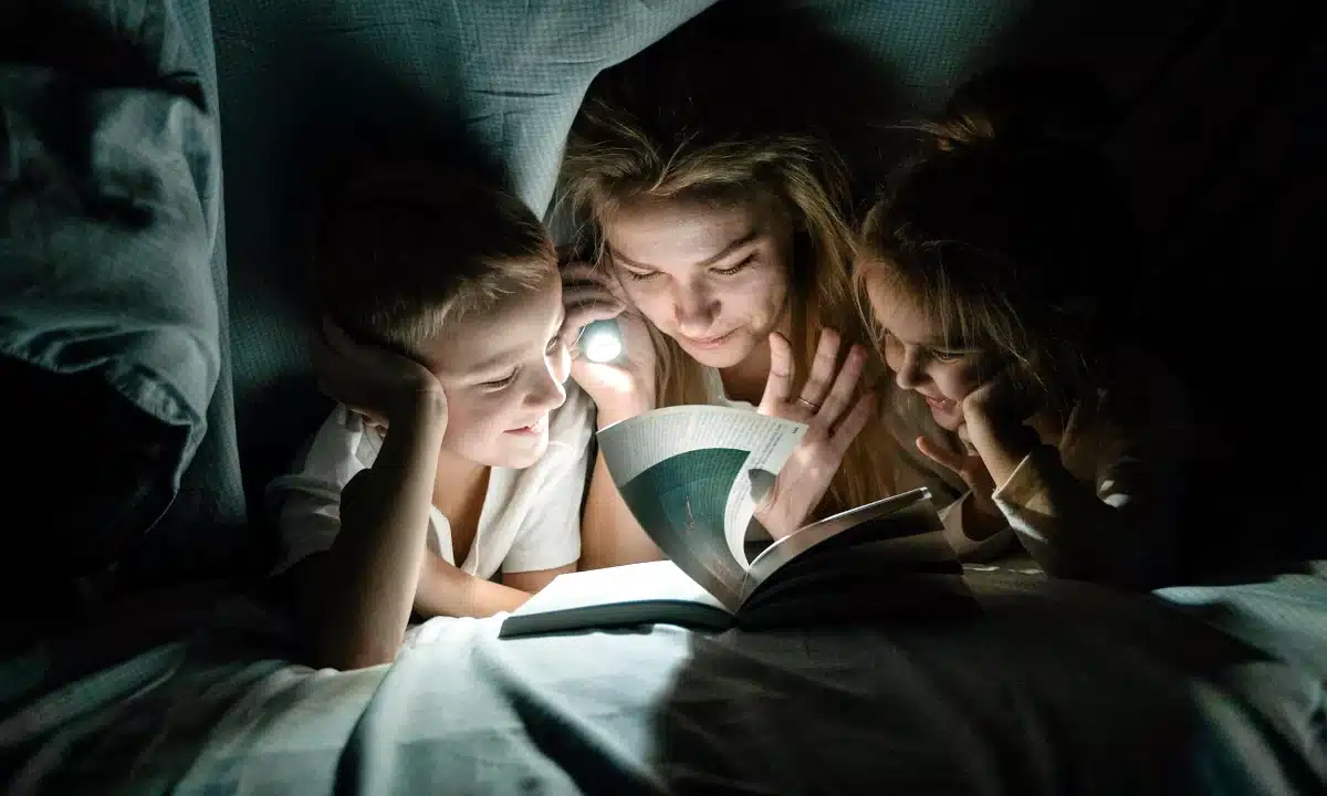 Мама з дітьми читають книжку з ліхтариком.