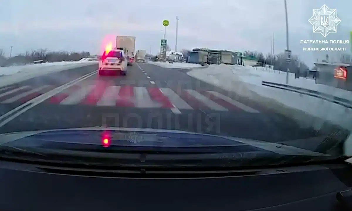 Патрульне авто із включеними маяками їде позаду вантажівки.