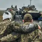 У Рівному навчатимуть, як без бар’єрів спілкуватися з ветеранами після фронту Поранений військовий йде спираючись на плече побратима на фоні військвої техніки.