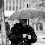 Чоловік з парасолею на вулиці міста, падає сніг.