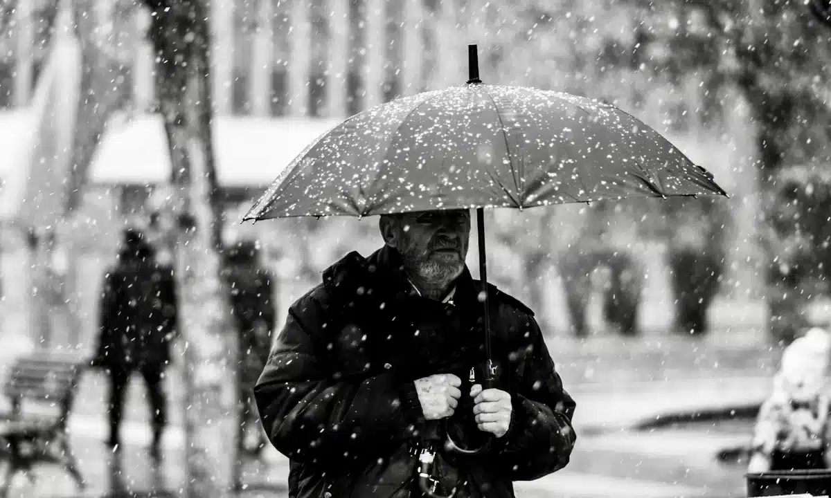 Чоловік з парасолею на вулиці міста, падає сніг.