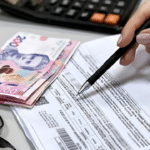 Оформити субсидію у Рівному тепер можна ще за однією адресою Оформлення документів на субсидію: рука з ручкою заповнює бланк, поруч лежать гривневі купюри та калькулятор.