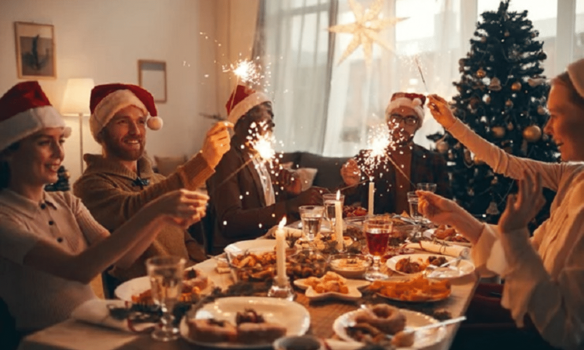 Як відновити організм після свят без крайнощів і шкоди здоров’ю Святкова вечеря вдома: родина та друзі за різдвяним столом із святковими стравами, ялинкою та бенгальськими вогнями.