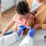 Лікарка заклеює місце вакцинації на руці дівчинки.