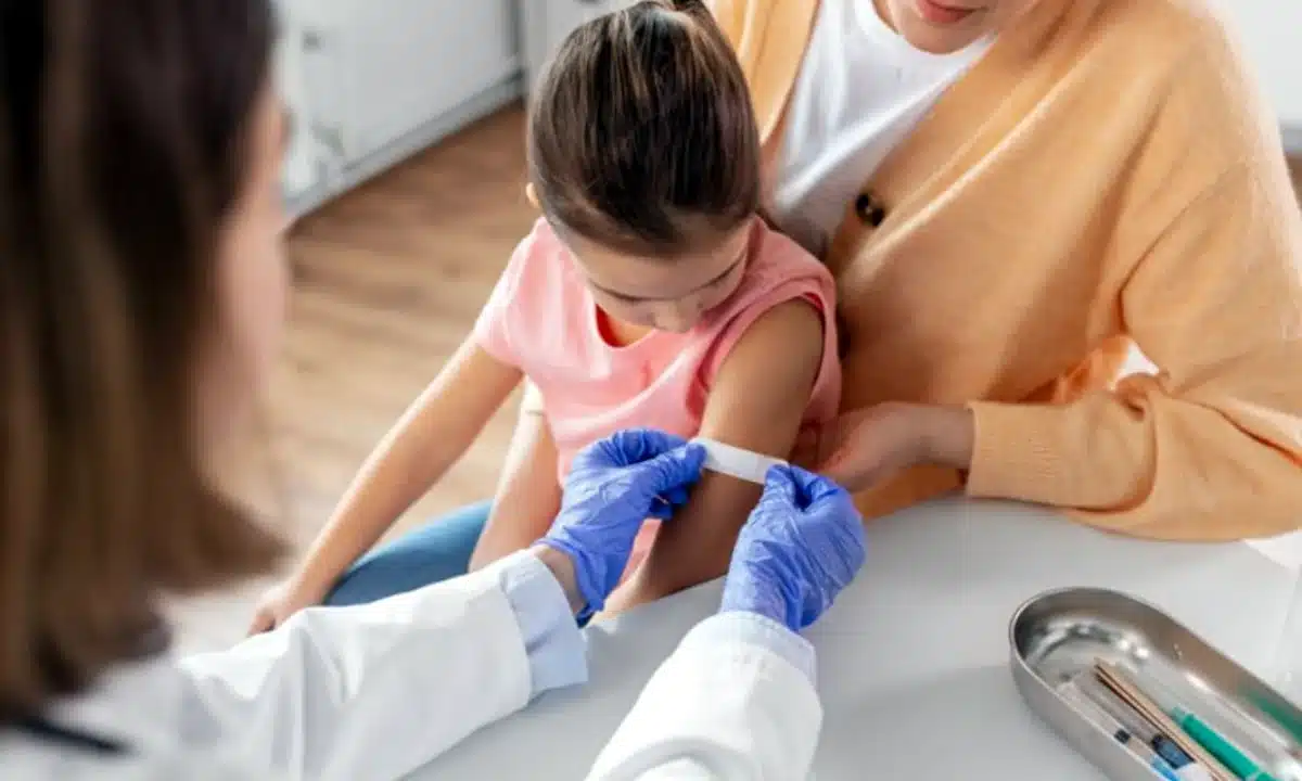 Лікарка заклеює місце вакцинації на руці дівчинки.