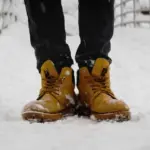 Чоловік стоїть у зимовому взутті на снігу.