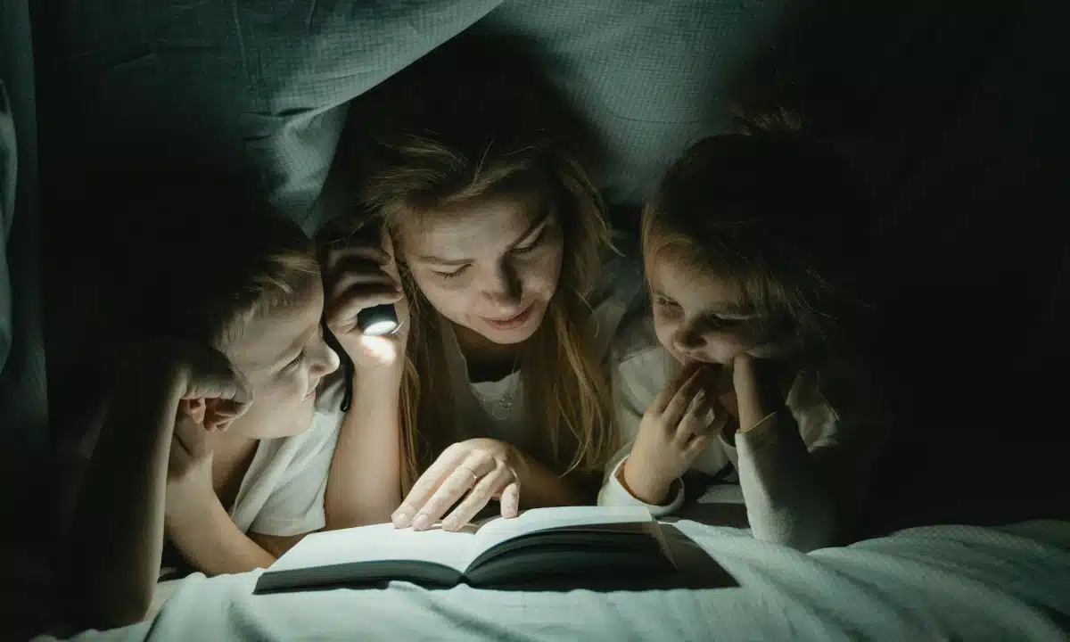 Мама з дітьми читають книжку з ліхтариком.