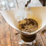 Заварювання фільтр-кава: гарячу воду наливають через паперовий фільтр із меленою кавою в ручній кавоварці на дерев&rsquo;яному столі