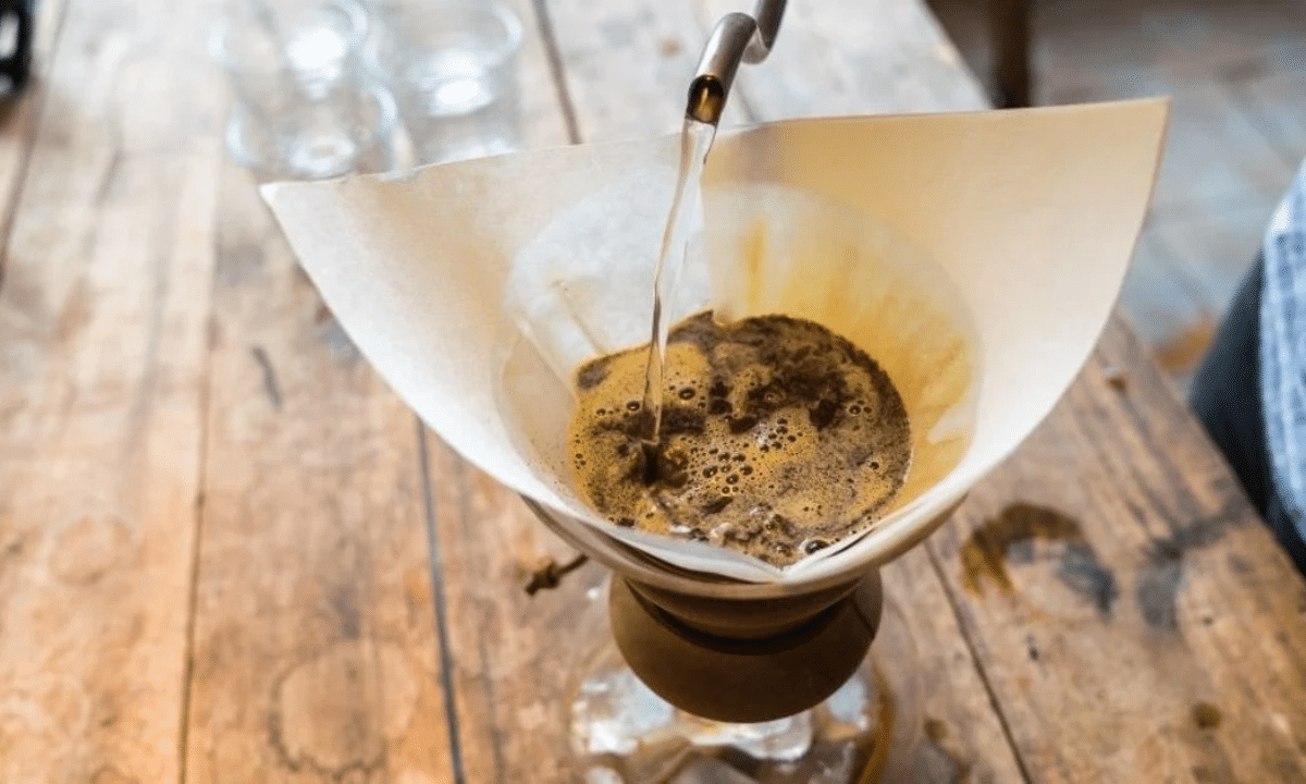 Як краще заварювати каву, щоб не підвищувати холестерин Заварювання фільтр-кава: гарячу воду наливають через паперовий фільтр із меленою кавою в ручній кавоварці на дерев’яному столі