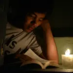 Хлопець читає книжку при свічці.