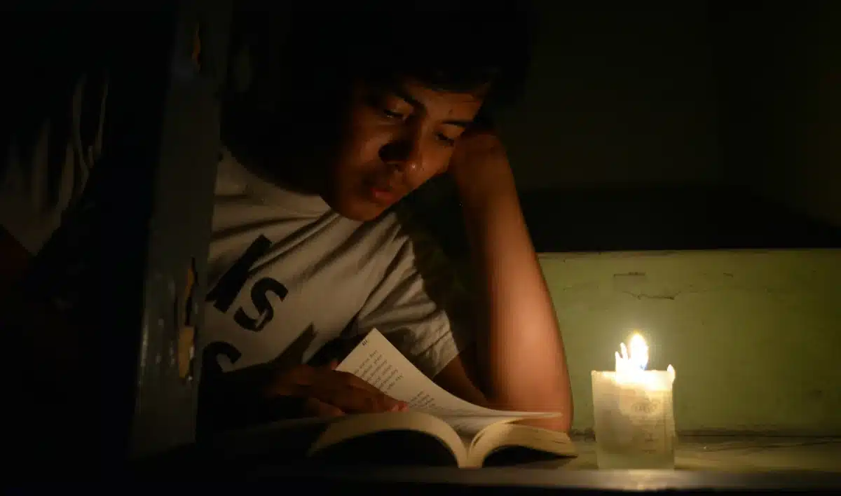 Хлопець читає книжку при свічці.