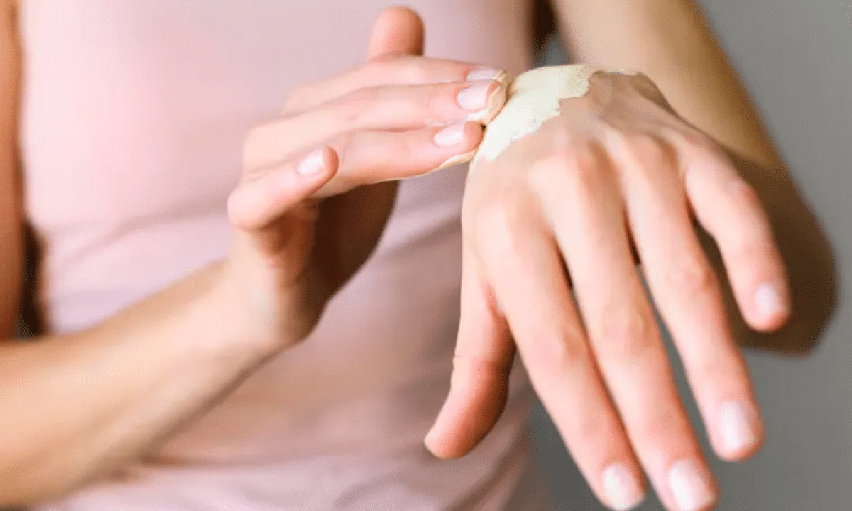 Суха шкіра рук-жінка наносить зволожувальний крем на тильну сторону руки.