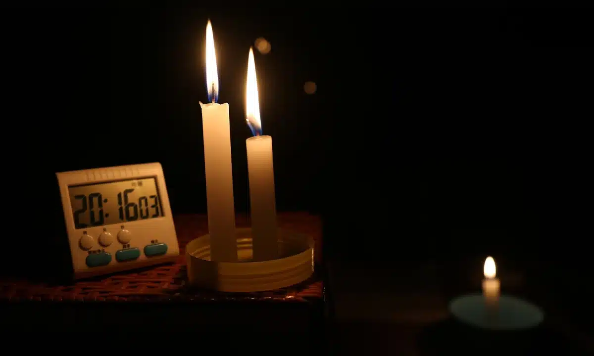 Графіки відключень електроенергії на Рівненщині у вівторок, 3 лютого На столі горять три свічки, поряд годинник.