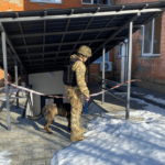 Поліцейський вибухотехнік із службовим собакою перевіряє вхід до підвального приміщення біля будівлі під час реагування на повідомлення про замінування.