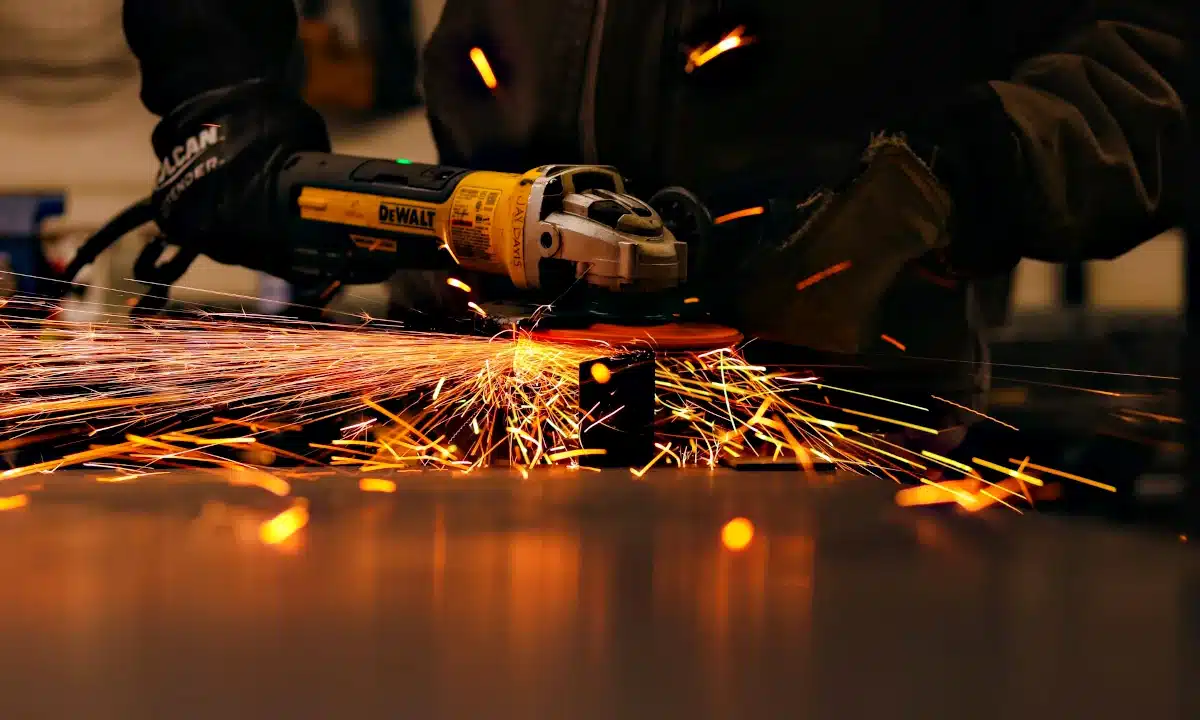 Слюсар зачищає болгаркою деталь.