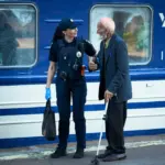Поліцейська йде з евакуйований пенсіонером біля потяга.